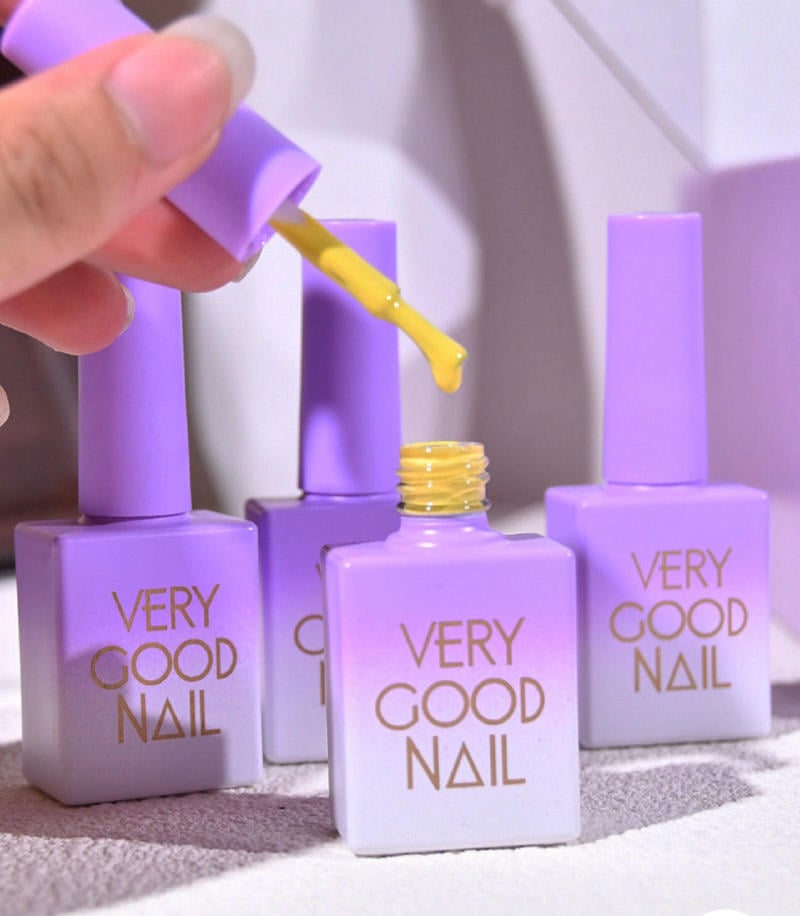 bang-mau-very-good-nail__14__2cff924f7f684d718b6696e5d7ec64d3 Lọ sơn móng tay màu tím với cọ sơn màu vàng đang được lấy ra. Nền trắng và bóng.