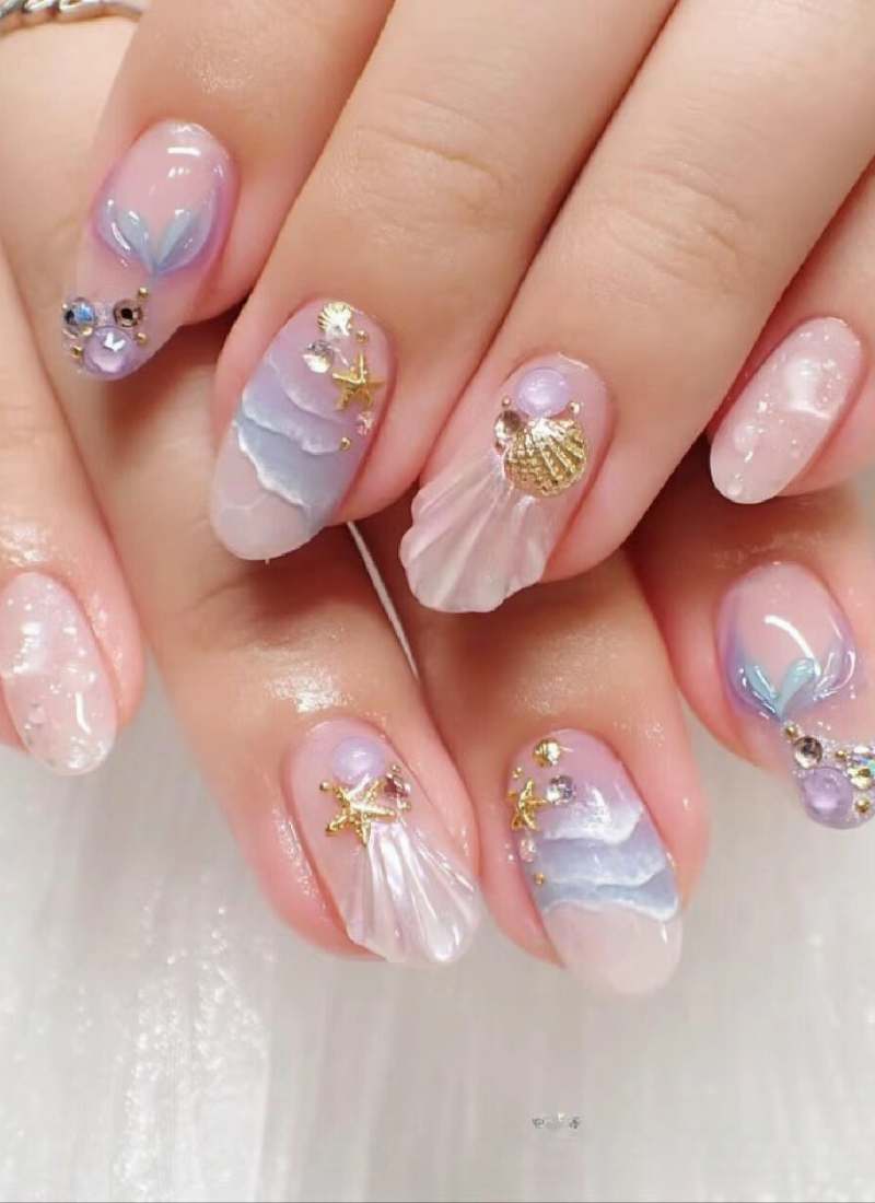 Bộ móng tay được trang trí với họa tiết vỏ sò, ngọc trai và ngôi sao biển trên nền màu pastel nhẹ nhàng.