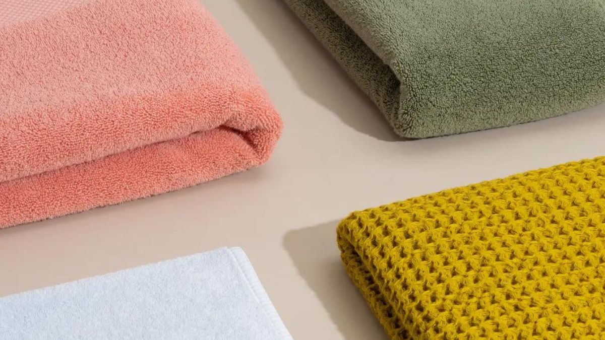 Bốn chiếc khăn tắm màu sắc khác nhau (hồng, xanh lá, xám, vàng) được gấp gọn trên mặt phẳng.