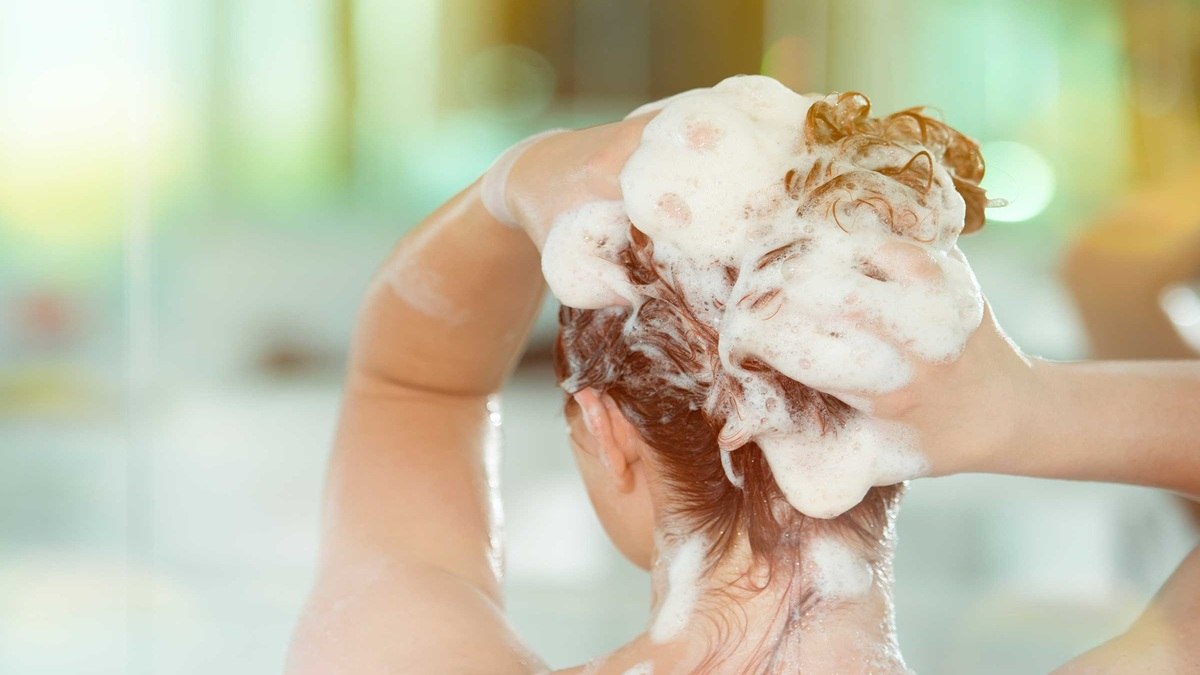 Người đang gội đầu, tóc đầy bọt xà phòng, trong bối cảnh phòng tắm sáng sủa.