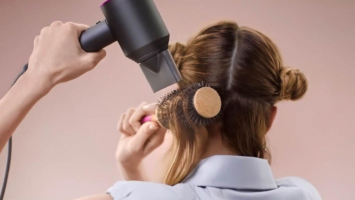Người đang sấy tóc với máy sấy và lược tròn, tóc được chia thành từng phần để tạo kiểu.