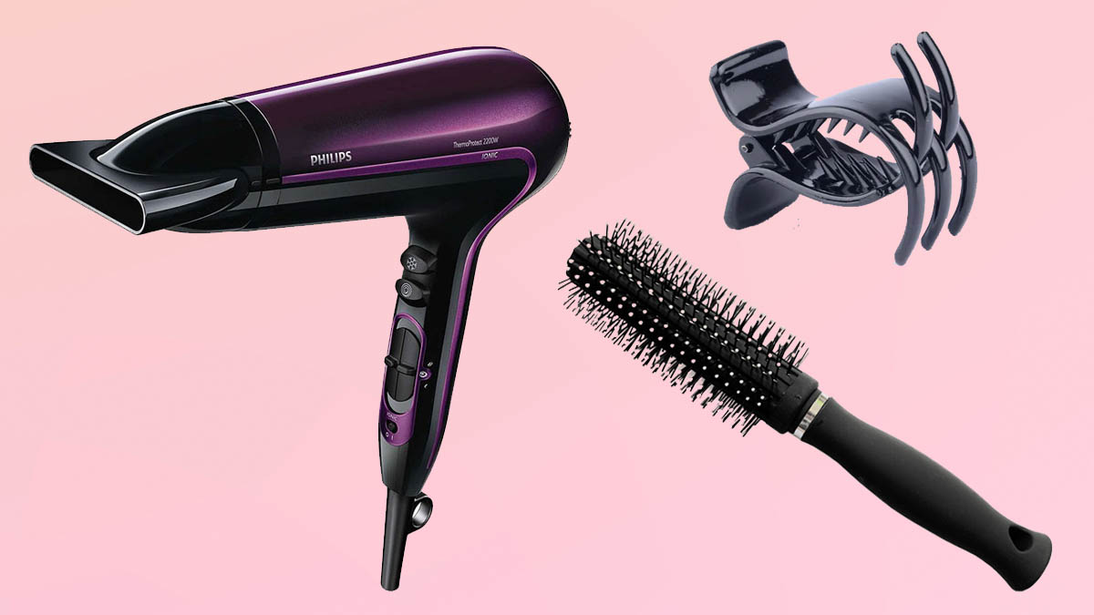 Máy sấy tóc, kẹp tóc và lược tròn trên nền hồng.