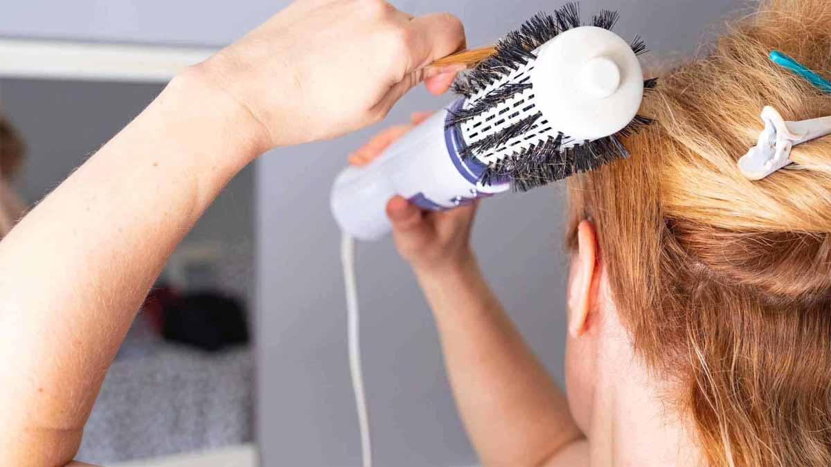 Người đang sử dụng lược xoay và máy sấy tóc để tạo kiểu tóc trong phòng.