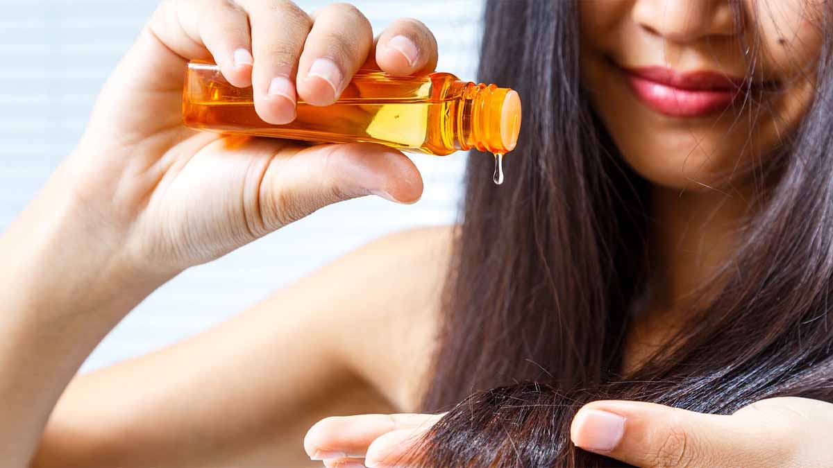 Người phụ nữ đổ dầu từ chai màu cam lên tay và tóc, tập trung vào chăm sóc tóc.