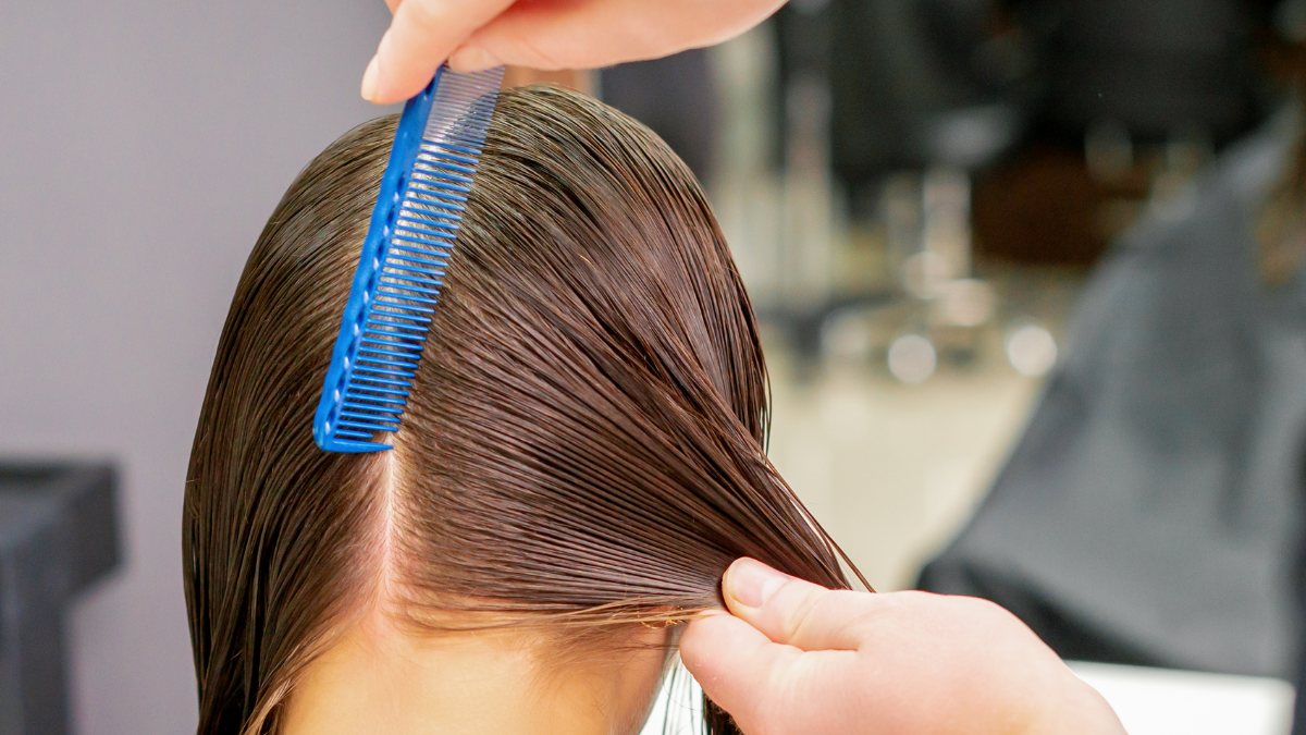 Người thợ dùng lược chải tóc ướt cho một người trong tiệm làm tóc, tóc được chia thành từng phần đều.