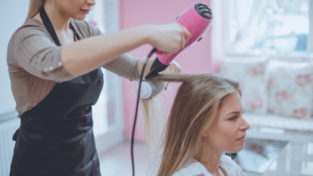 Người thợ làm tóc đang sấy và tạo kiểu tóc cho khách hàng trong tiệm salon.