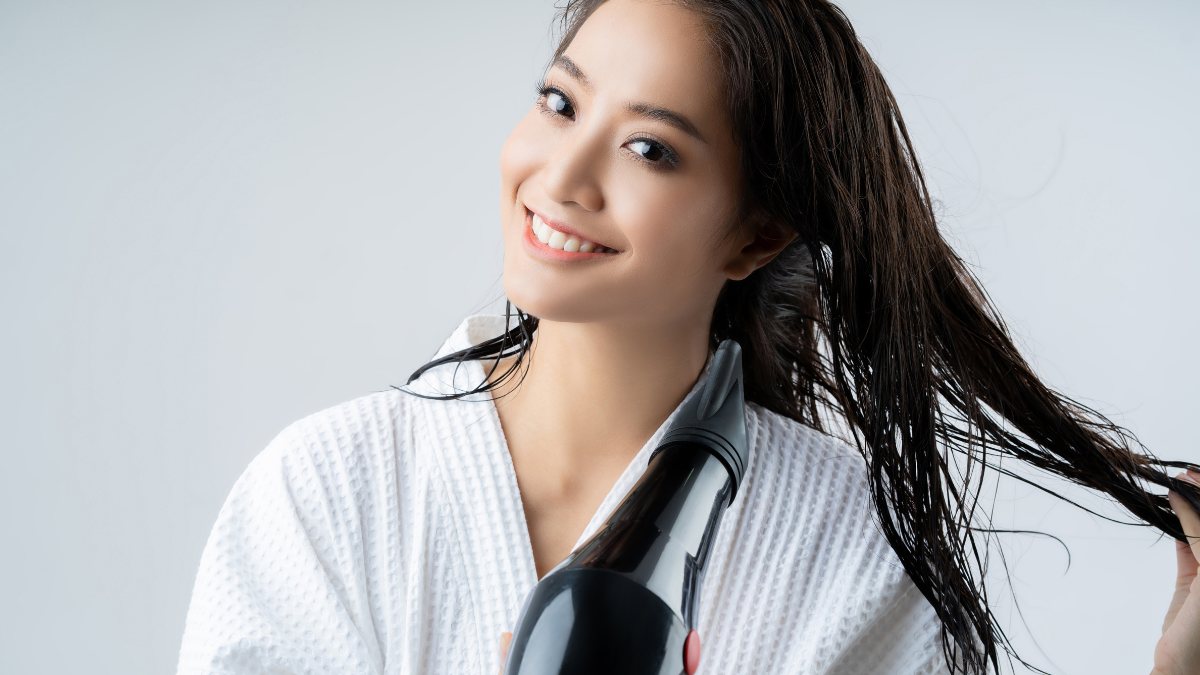 Người mặc áo choàng trắng đang sấy tóc bằng máy sấy, tạo kiểu tóc trong môi trường sáng sủa.