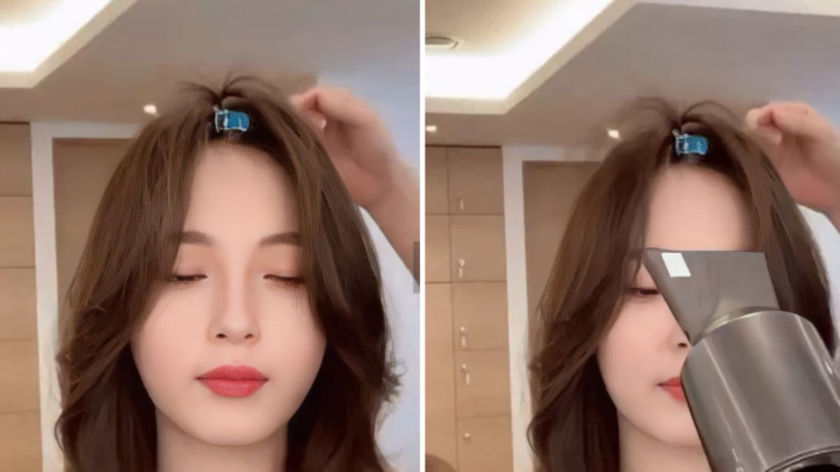 Người phụ nữ nhắm mắt, tóc được kẹp bằng kẹp xanh, đang sấy tóc trong phòng sáng.