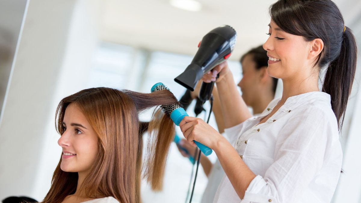 Người thợ làm tóc đang sấy và chải tóc cho khách hàng bằng máy sấy và lược tròn trong tiệm làm tóc.