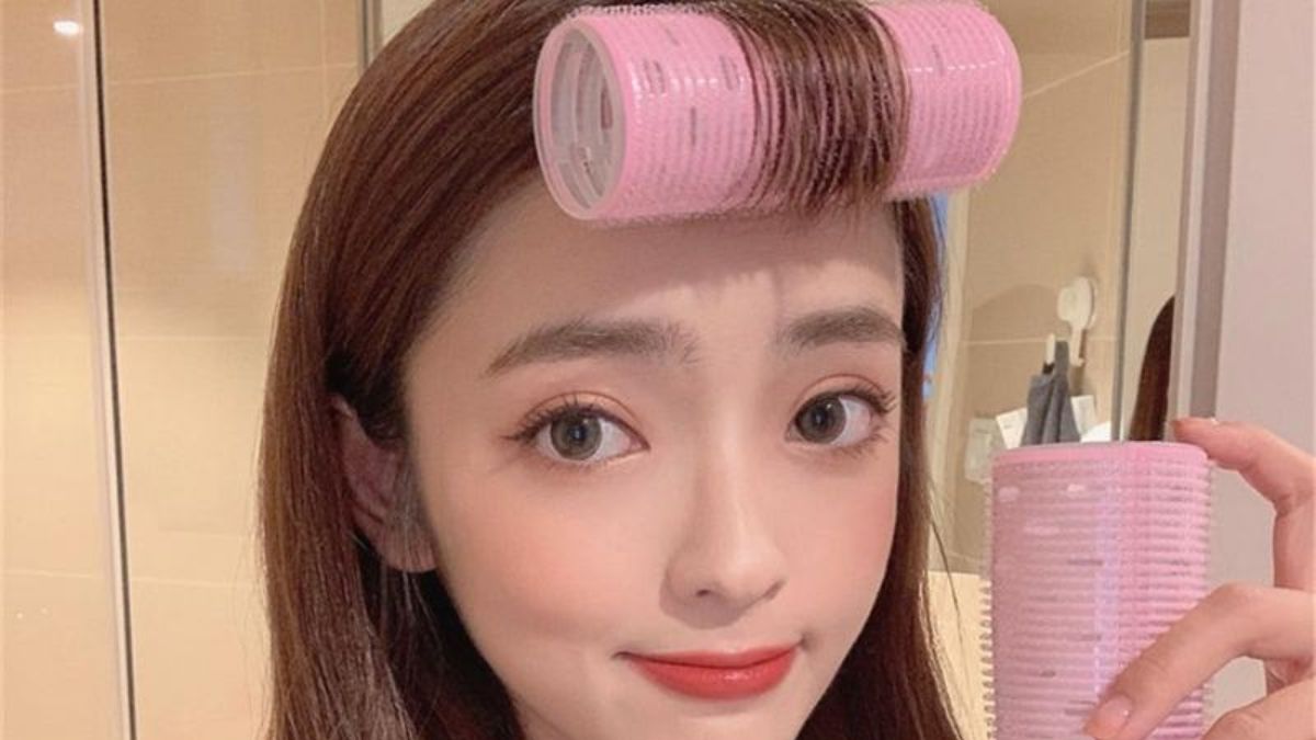 Người cầm lô cuốn tóc hồng, một cái trên tóc và một cái trong tay, trong phòng có gương.