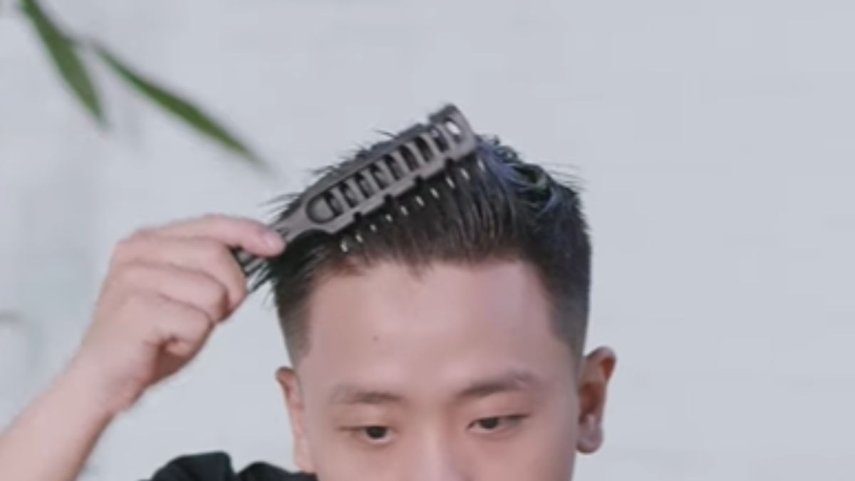 Người đàn ông dùng lược chải tóc, nền phía sau là tường sáng màu.
