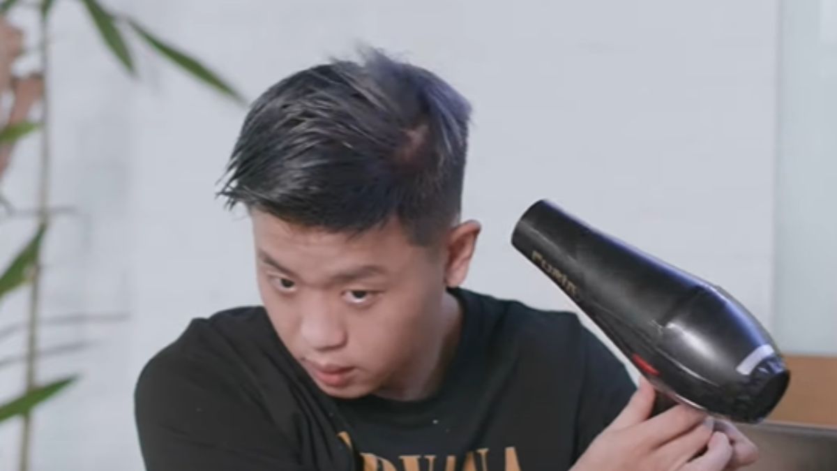 Người đàn ông đang sử dụng máy sấy tóc để làm khô tóc trong không gian nội thất.