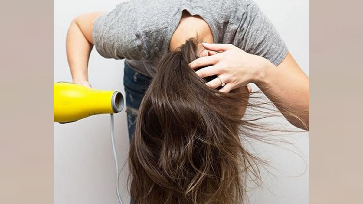 Người đang sấy tóc bằng máy sấy màu vàng, nghiêng đầu xuống để tạo kiểu cho tóc.