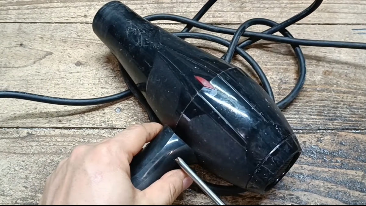 Máy sấy tóc màu đen đang được một tay cầm, đặt trên bề mặt gỗ.