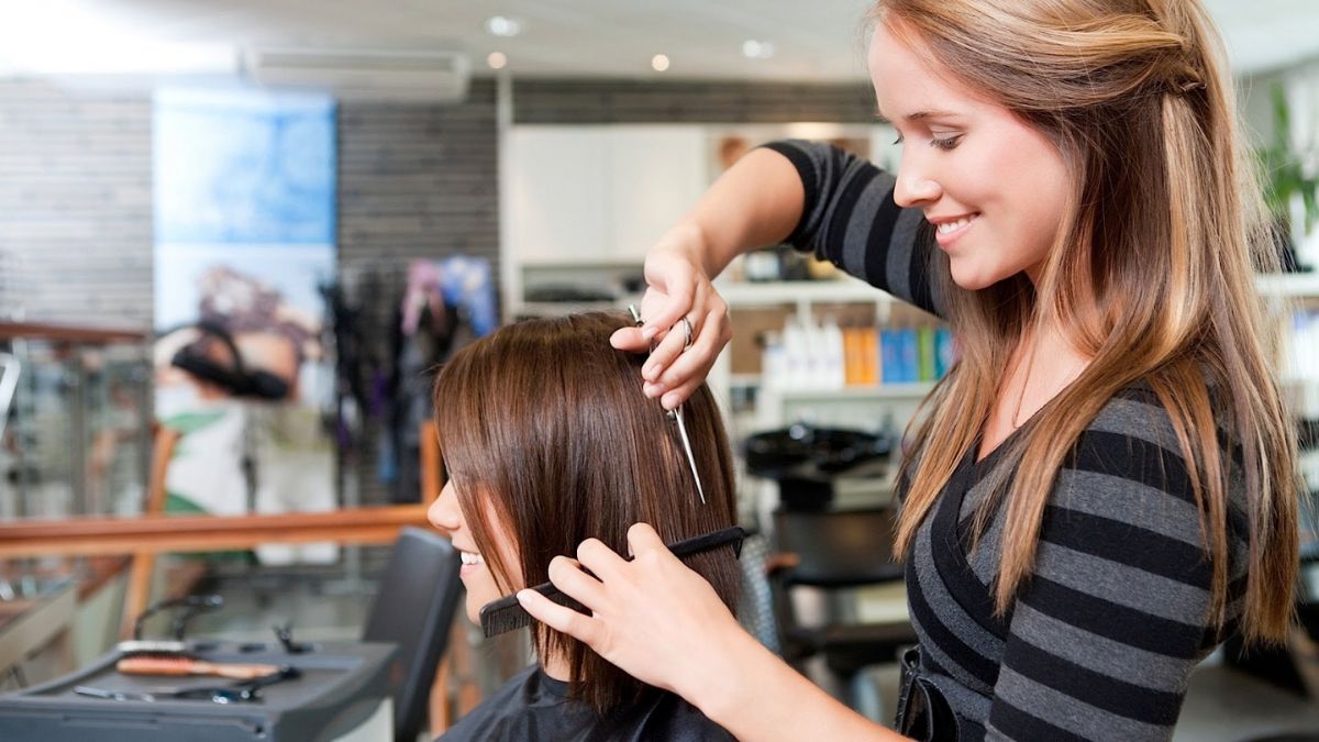Nhà tạo mẫu tóc đang cắt tóc cho khách hàng trong tiệm làm tóc sáng sủa và hiện đại.