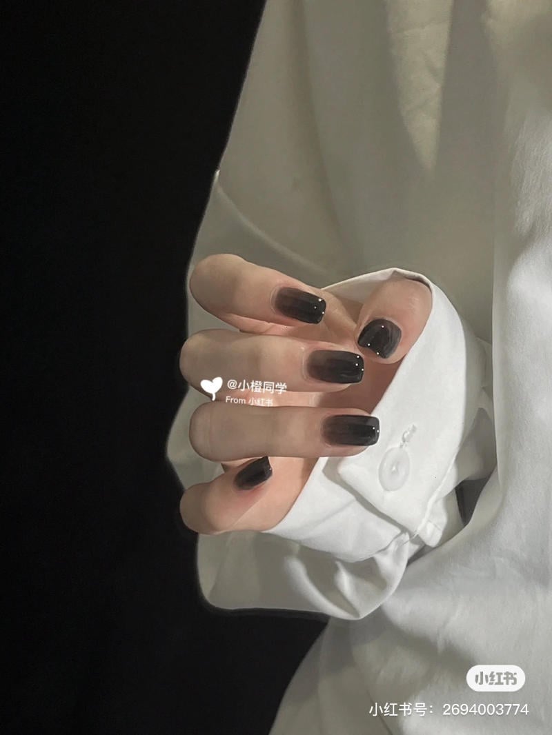 Bàn tay với móng tay sơn đen, mặc áo sơ mi trắng, trên nền đen.