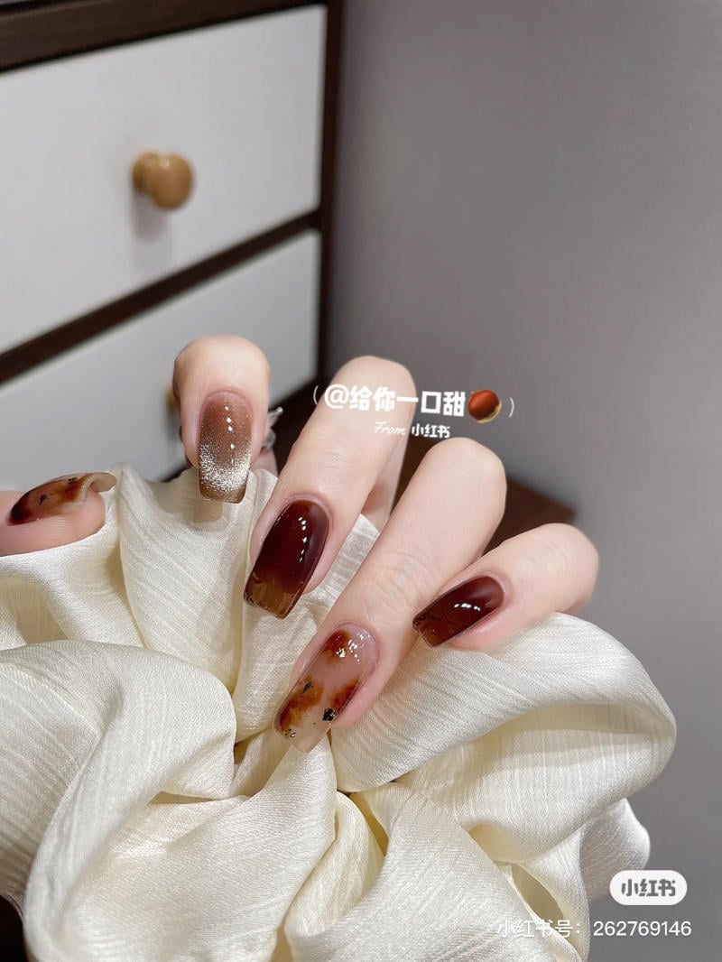 Bàn tay với móng tay được sơn màu nâu, cầm một dây chun vải màu trắng, nền là tủ gỗ.