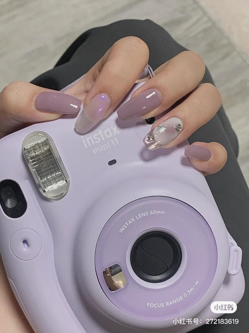 Người cầm máy ảnh Instax Mini 11 màu tím, móng tay được sơn màu tím nhạt và trang trí đá.