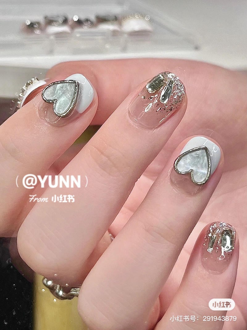 Bàn tay với móng tay được trang trí bằng hình trái tim và kim tuyến lấp lánh trên nền trắng và trong suốt.