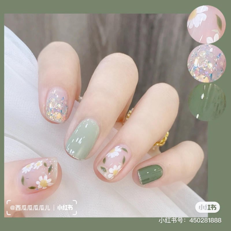 Bàn tay với móng tay được sơn màu xanh lục và hoa văn trang trí hình hoa cúc và kim tuyến lấp lánh.
