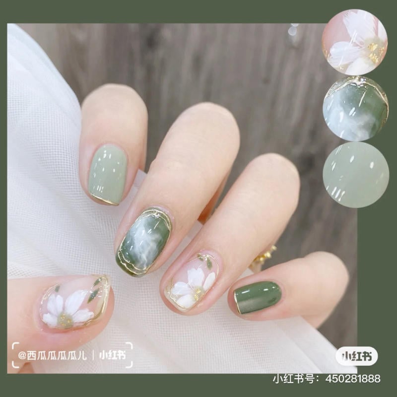 Bàn tay với móng tay được trang trí họa tiết hoa và màu xanh, nền vải trắng.