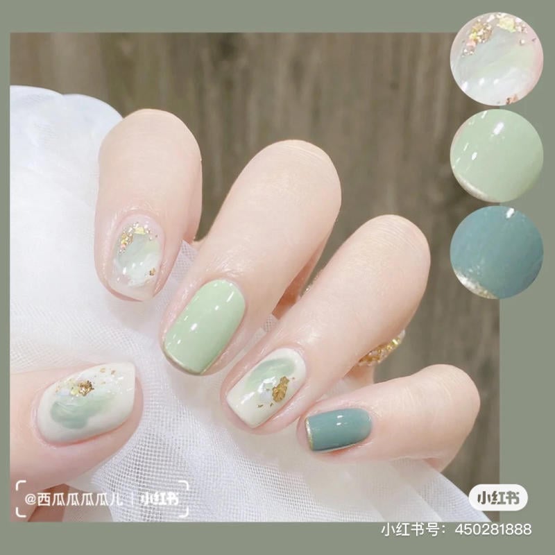 Bàn tay với móng tay sơn màu xanh và trắng, trang trí họa tiết vàng và xanh nhạt.