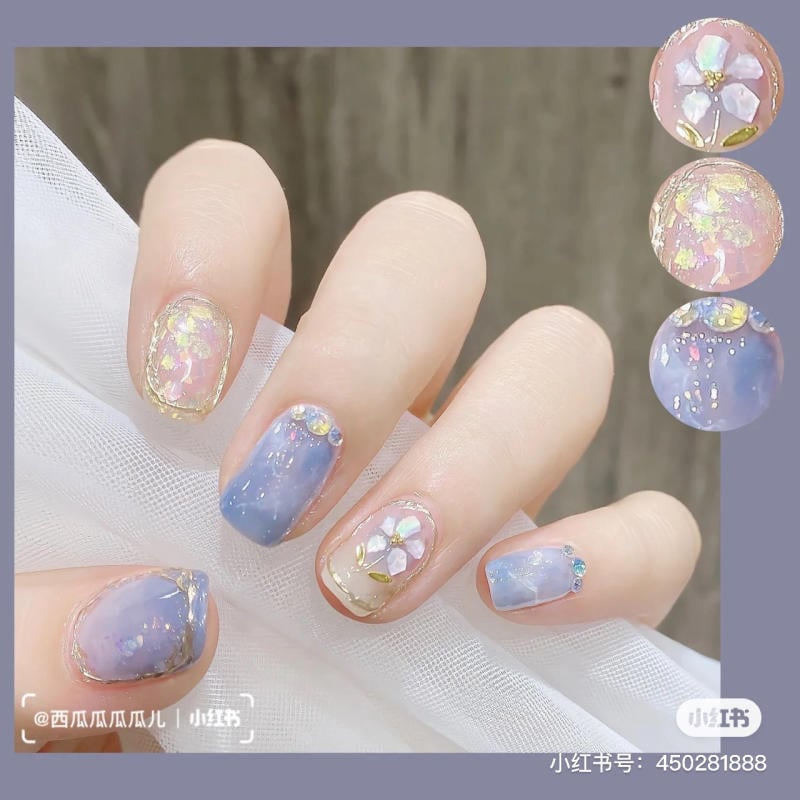 Bàn tay với móng tay được trang trí hoa và màu sắc pastel, kết hợp hiệu ứng lấp lánh và đá quý nhỏ.