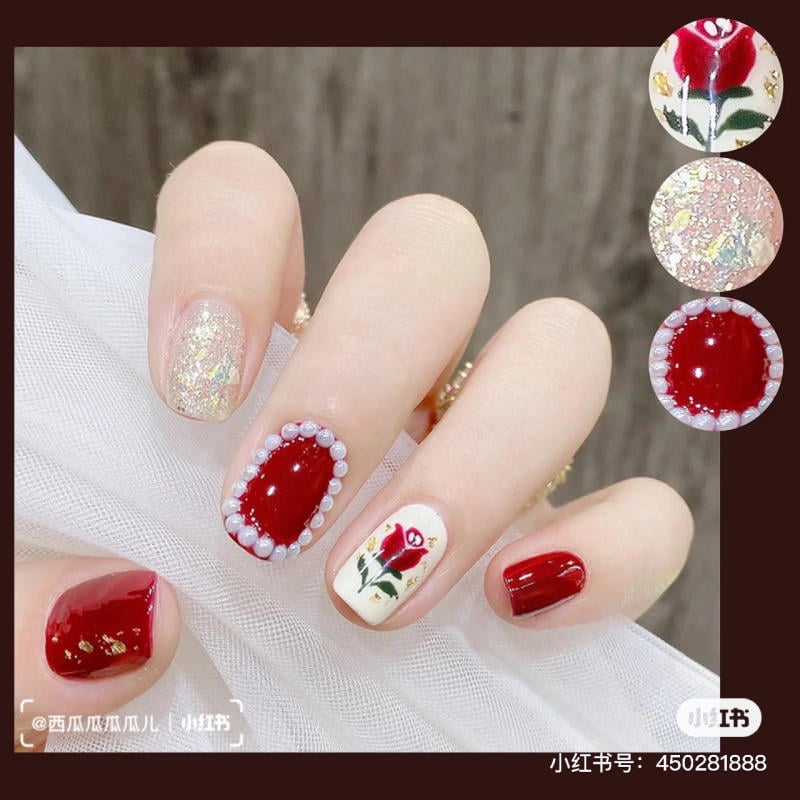 Bàn tay với móng tay sơn đỏ và trắng, họa tiết hoa hồng và trang trí lấp lánh.