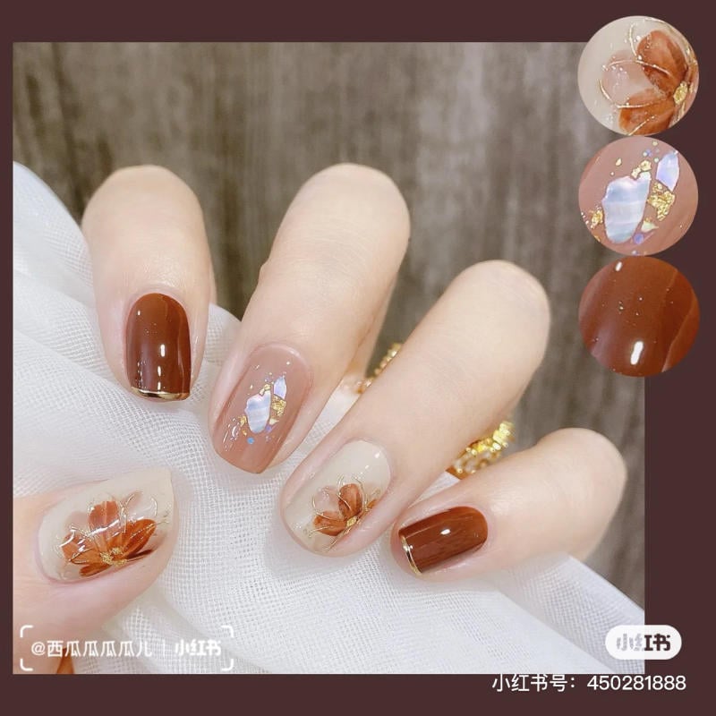 Bàn tay với móng tay sơn màu nâu và be, có họa tiết hoa và ánh kim loại.