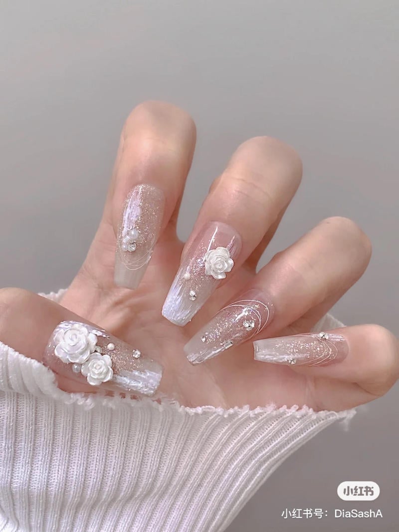 Bàn tay với móng tay dài được trang trí hoa và họa tiết trắng, mặc áo len trắng.
