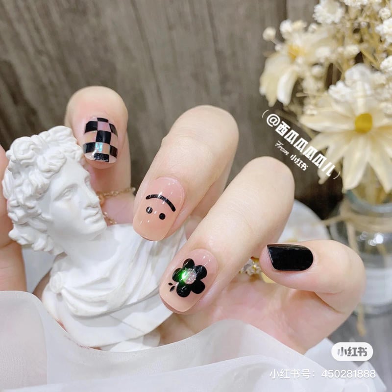 Bàn tay với móng tay trang trí họa tiết đa dạng, bên cạnh tượng bán thân trắng, nền có hoa và đồ trang trí.