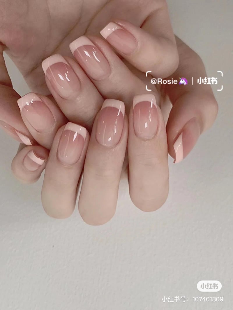 Bàn tay với móng được sơn kiểu Pháp, nền hồng nhạt và đầu móng trắng, chụp trên nền trắng.