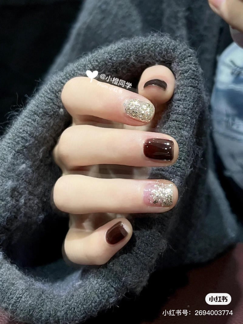 Bàn tay với móng tay sơn nâu và nhũ lấp lánh, áo len xám bao quanh.