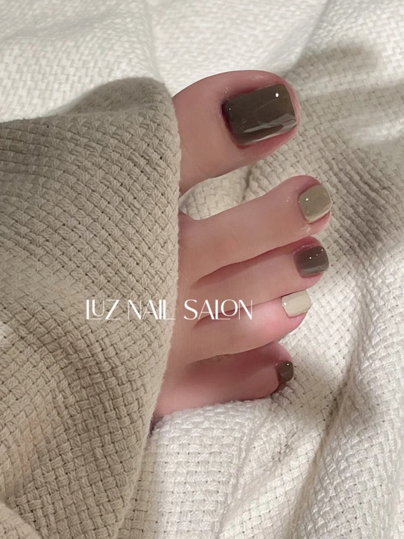 Bàn chân với móng chân được sơn màu xanh lá và be, đặt trên nền vải có kết cấu dệt.