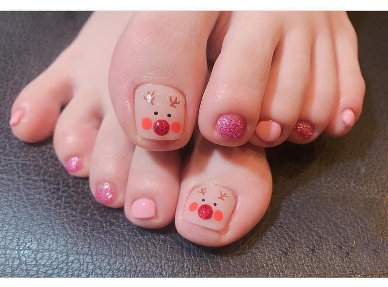 mau-nail-chan-noel__2__581ee99d1c2f497eb1493f7f5dd92e73 Bàn chân với móng trang trí hình tuần lộc và sơn màu hồng ánh kim trên nền da tối màu.