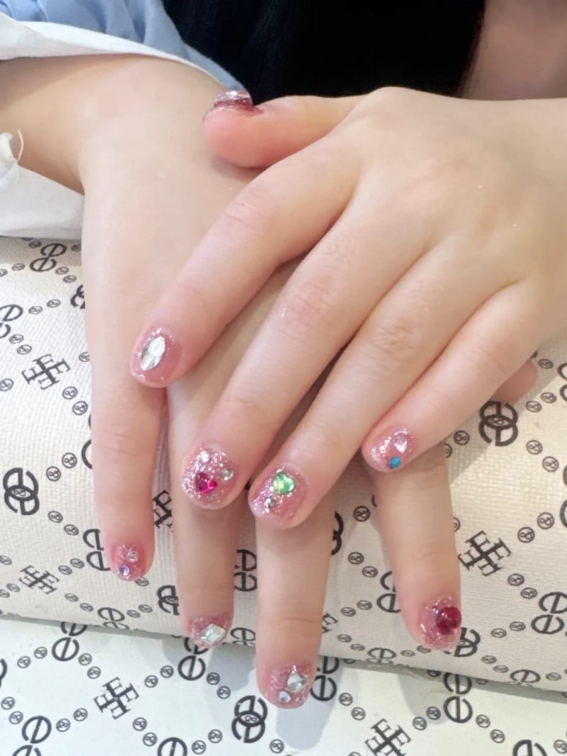Bàn tay với móng tay được trang trí bằng sơn lấp lánh và đính đá nhiều màu, đặt trên gối có hoa văn.