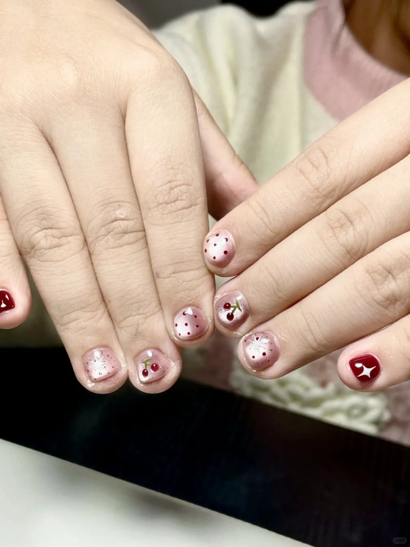 Bàn tay với móng tay được sơn màu đỏ, trang trí chấm bi và họa tiết hoa quả.