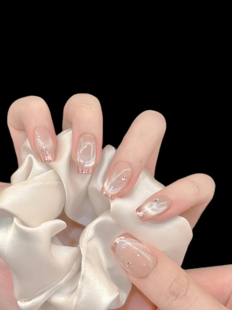Bàn tay với móng tay trang trí họa tiết đơn giản, cầm một chiếc dây buộc tóc bằng vải satin màu trắng.