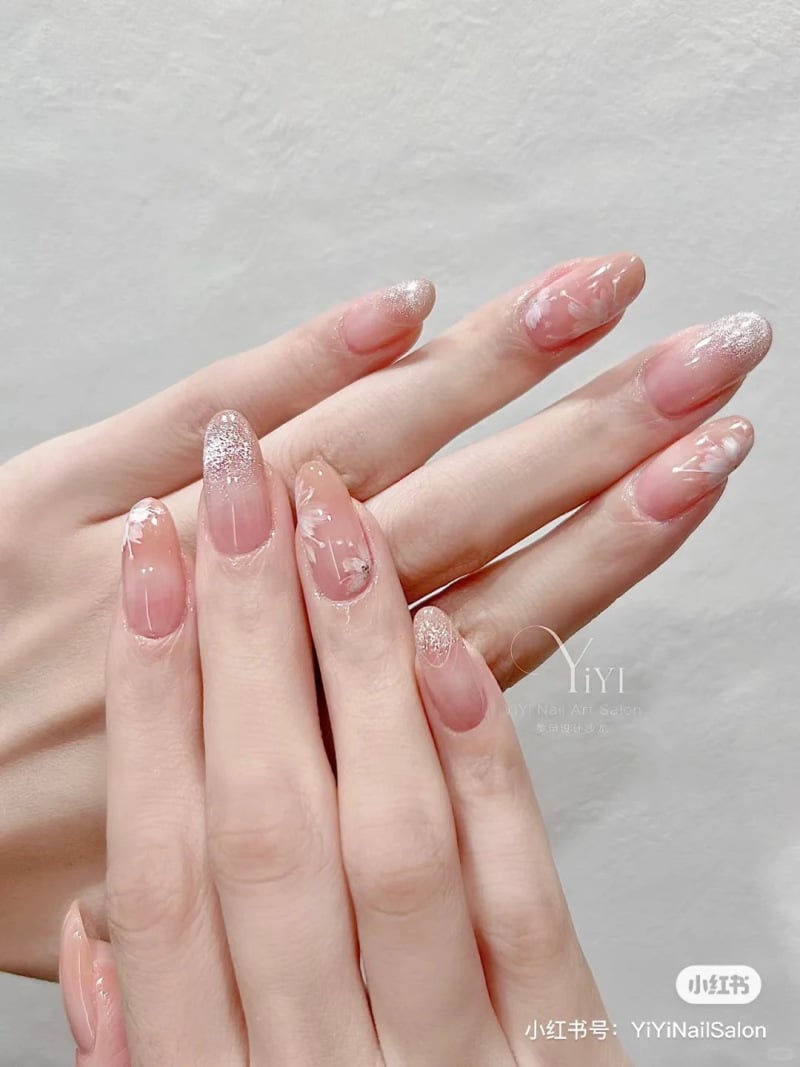 Bàn tay với móng tay được trang trí họa tiết lấp lánh và hoa văn tinh tế trên nền màu hồng nhạt.