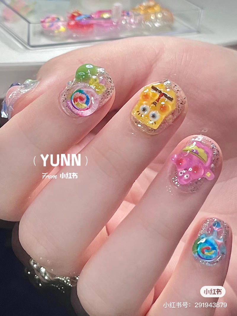Bàn tay với móng tay đính hình vẽ hoạt hình và họa tiết màu sắc nổi bật.