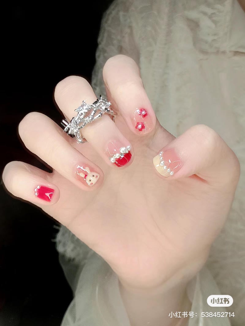 Bàn tay đeo nhẫn bạc với móng tay được trang trí hoa văn và màu sắc đa dạng, nổi bật với chi tiết ngọc trai nhỏ.