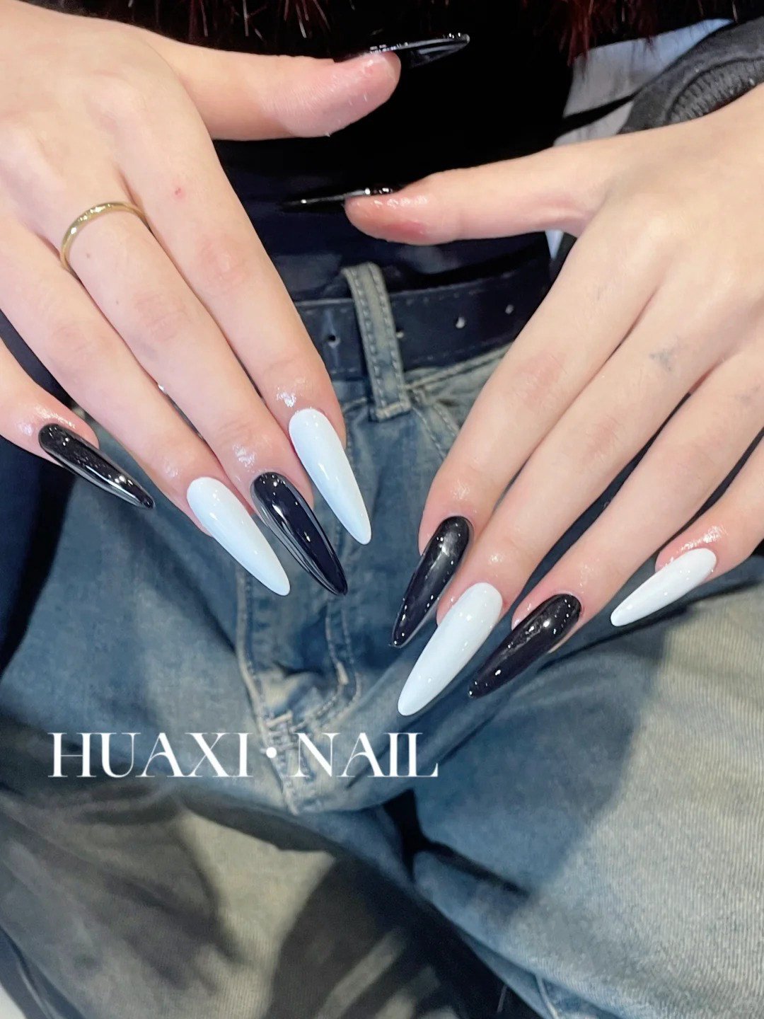 Bàn tay với móng tay dài được sơn màu đen và trắng xen kẽ, đặt trên nền quần jean.