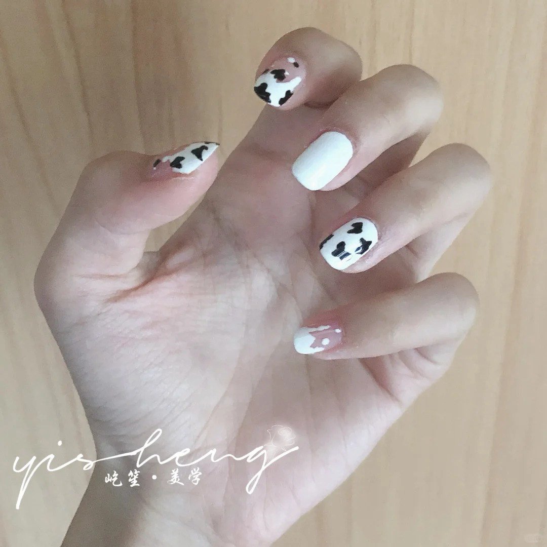 Bàn tay với móng tay được sơn họa tiết đen trắng giống da bò và màu trắng.