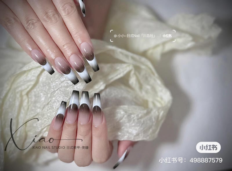 Bàn tay với móng tay dài được sơn ombre trắng đen, trên nền vải trắng nhạt.