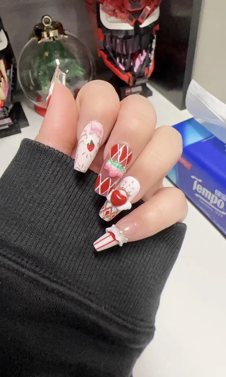 mau-nail-do-trang-cardina-7-jpg_77f23796628f454ba462fba6e86e3bdb Bàn tay với móng tay được trang trí cầu kỳ, họa tiết trái cây và sọc đỏ trắng, tay áo màu đen.