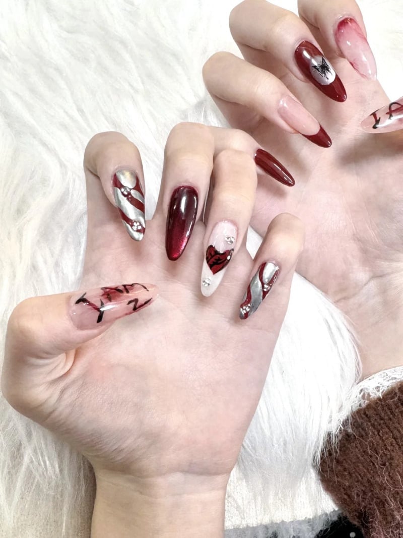 mau-nail-do-trang-cardina-9-jpg_4bada8218c6e4cd1bb4190bec73d86cc Bàn tay với móng tay dài, sơn màu đỏ và trắng, có họa tiết trang trí phức tạp trên nền trắng.