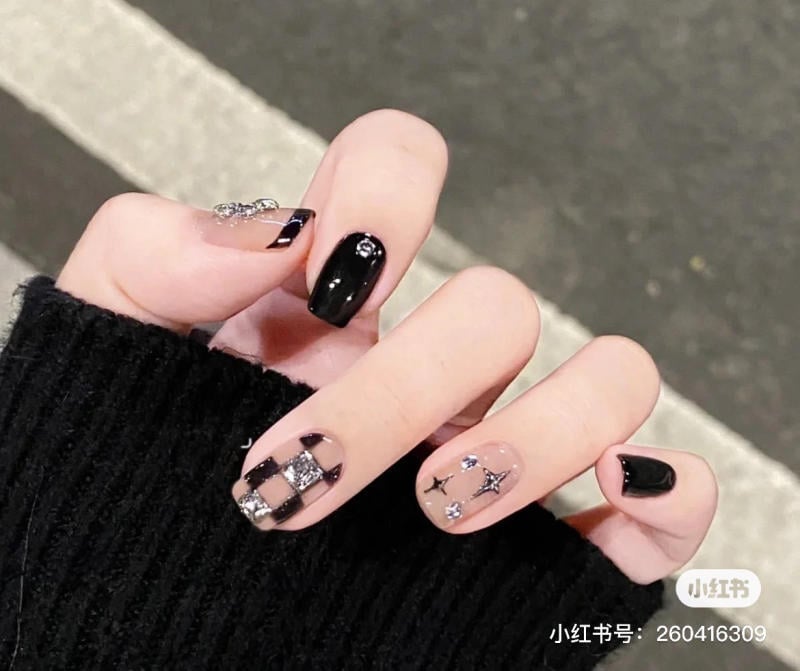 mau-nail-don-gian-cardina__104__ff150a6557954a318b6f48a8d9c0e28d Bàn tay với móng tay được trang trí họa tiết đen trắng và họa tiết ngôi sao, nền là mặt đường vỉa hè.