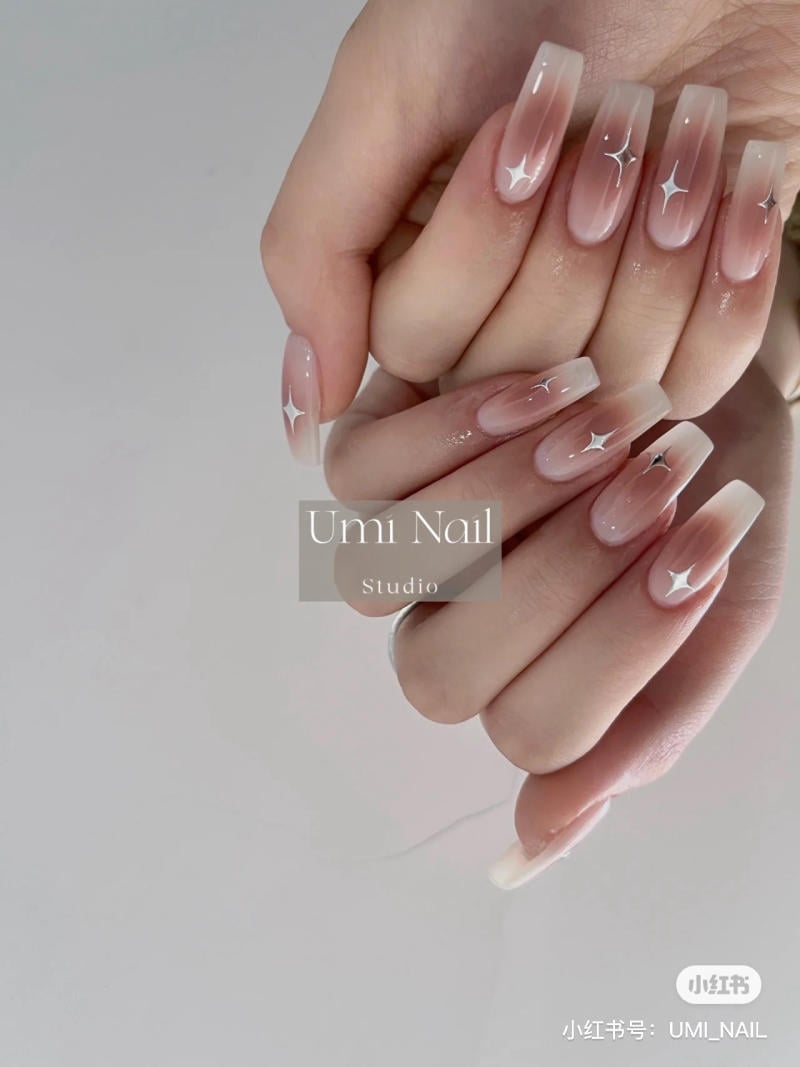 mau-nail-don-gian-cardina__110__a696df31ef994312af087a1c45377447 Bàn tay với móng tay dài sơn màu hồng nhạt ombre, trang trí họa tiết ngôi sao trắng.