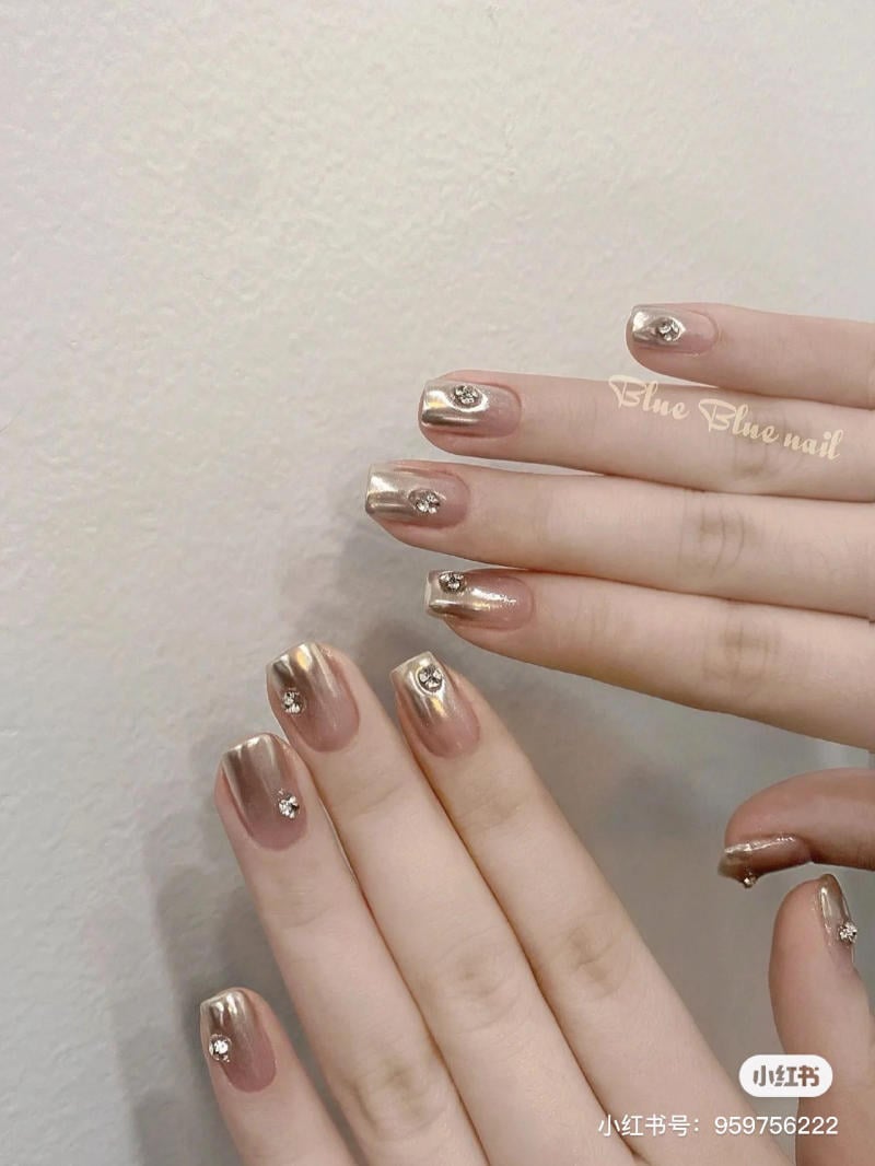 mau-nail-don-gian-cardina__140__c1097fb91b4a475b983bfe45f434e0b9 Bàn tay với móng tay sơn màu vàng ánh kim, trang trí đá lấp lánh, trên nền tường trắng.