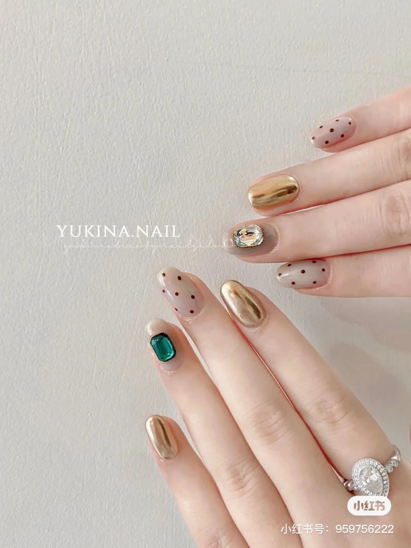mau-nail-don-gian-cardina__141__daec41537fb64bd8b667656753414ca5 Bàn tay với móng tay được sơn màu vàng ánh kim, chấm bi, đính đá xanh và nhẫn kim cương.